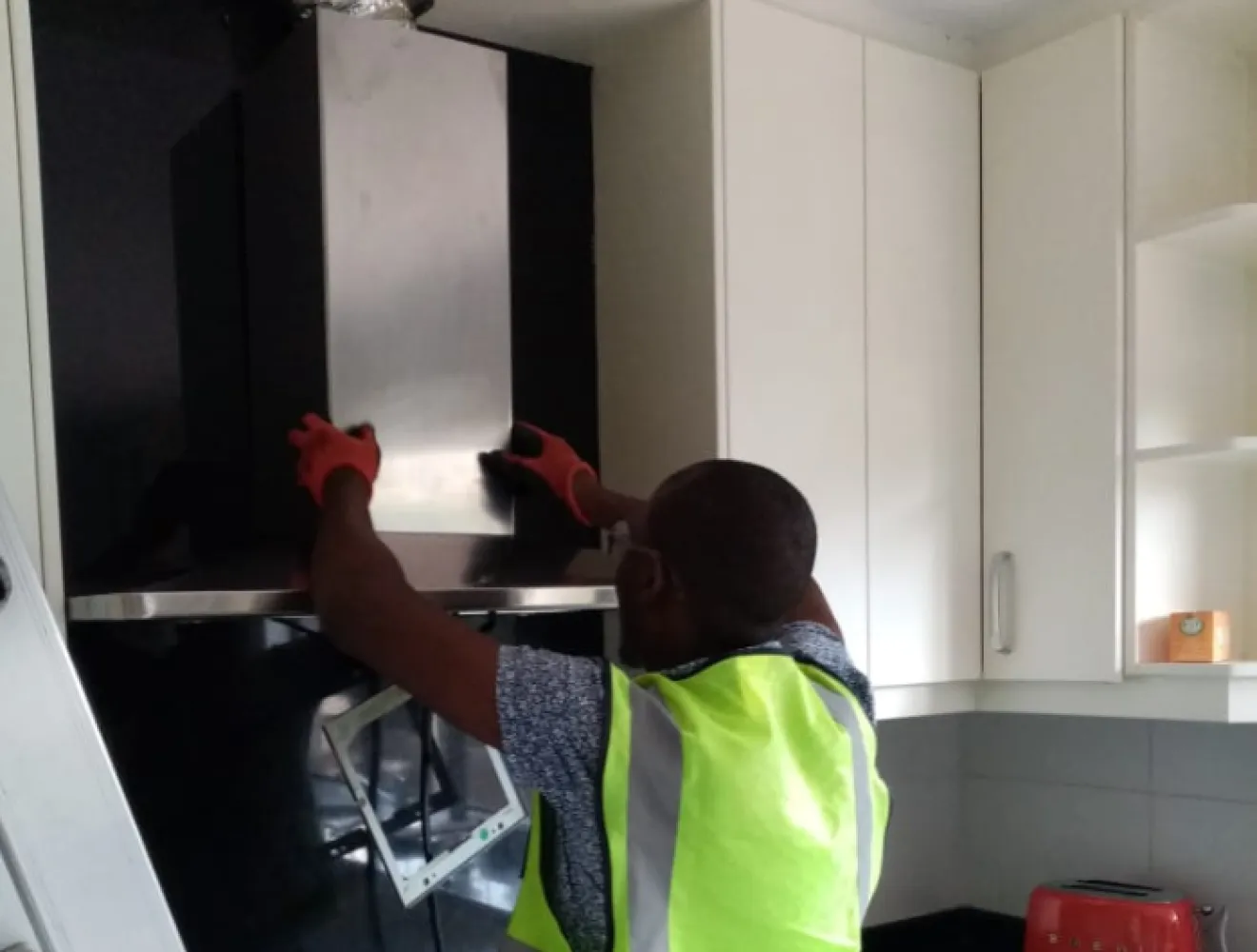 Technician fitting a cooker hood above a hob during an installation